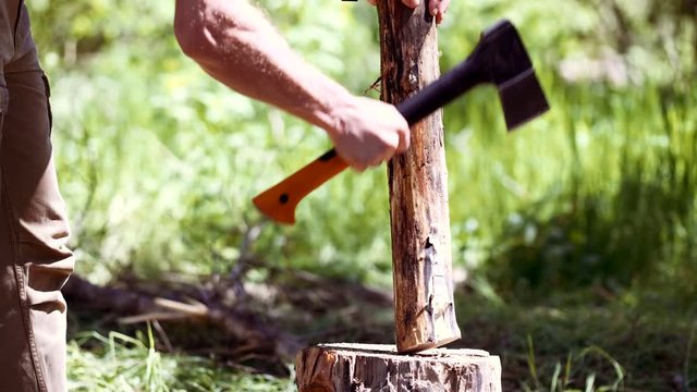 Lumberjack man chopping wood with axe in the forest outdoors. Explorer and traveler sharpens wooden timber stick for campfire on wild nature background. Man cutting tree branch, making firewood.
