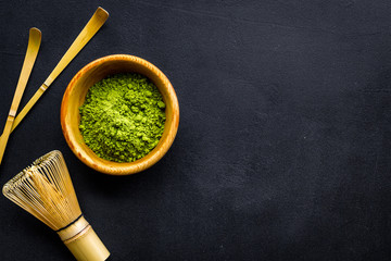 Japanese matcha tea tradition. Matcha accesories, whisk near matcha powder in bowl on black background top view copy space