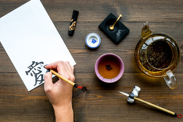 Calligraphy. Hand writes hieroglyph love on white paper on dark wooden background top view