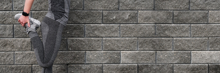 Fitness woman runner stretching legs before run on the wall.