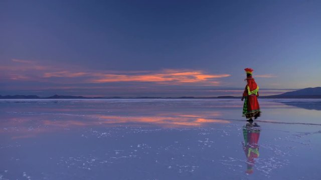 Bolivian woman at sunrise walking on the Salar de Uyuni Salt flats in Multi coloured traditional National clothing South America