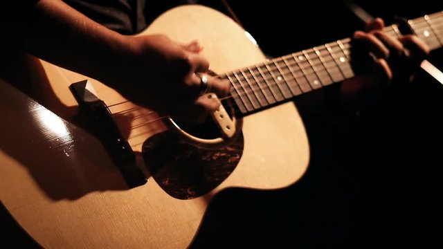 Male playing acoustic guitar on stage for a live performance. Strumming in slow motion