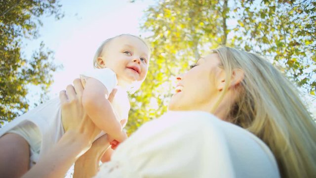 Smiling blonde young Caucasian mother holding her baby girl outdoors in the park 