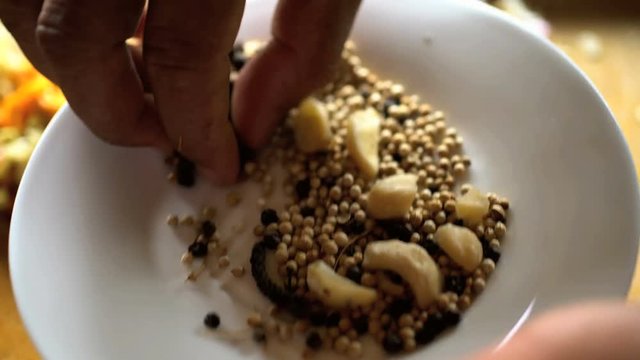 Hands adding seeds to ingredients on wooden chopping board in preparation of Basa gede in Balinese cooking class 