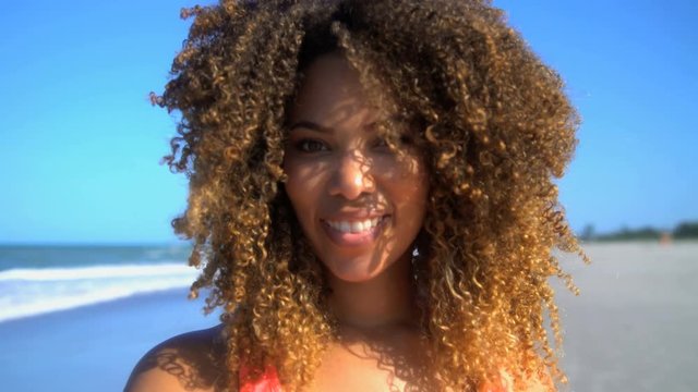 Portrait of attractive smiling African American female with afro hair chilling on their beach vacation