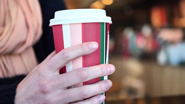 Clip taken at coffee shop cafe of a caucasian women picking up and setting down a holiday coffee shop cup with hot coffee or tea in it. Shot in 4k 60fps and slowed down to 50% on a 30fps timeline.
