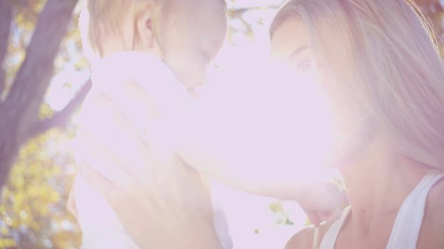 Attractive blonde young Caucasian mother bouncing her young baby boy in her arms outdoors in the park 