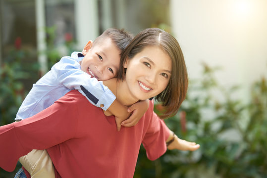 Young Asian Woman Giving Piggyback Ride To Her Little Son