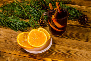 Cup of mulled wine with cinnamon, sliced orange and fir tree branches on wooden table