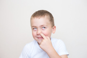 Little boy is picking his nose on a white background