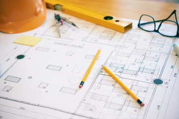 Pencils, glasses and construction level on table with building plan