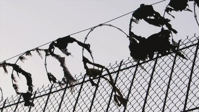 Tattered plastic and fabric is caught on some sketchy looking barbed wire. It races in the wind.