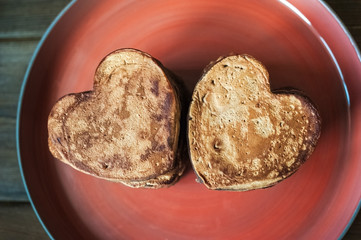 Heart-shaped chocolate pancakes on a red plate on a dark background. Breakfast for your beloved on Valentine's Day