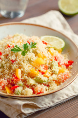 Couscous salad with fresh red and yellow bell peppers, avocado, tomatoes and lime. The concept of vegetarian and healthy food.