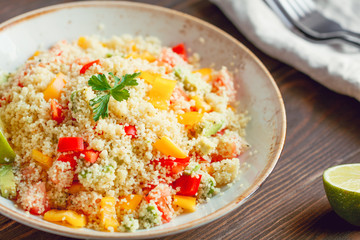 Couscous salad with fresh red and yellow bell peppers, avocado, tomatoes and lime. The concept of vegetarian and healthy food.