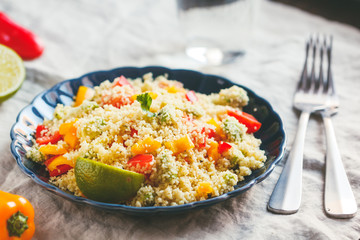 Couscous salad with fresh red and yellow bell peppers, avocado, tomatoes and lime. The concept of vegetarian and healthy food.