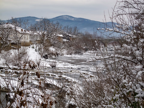 Picturesque snowy rural view to the winter Vidima River with the stone bridge in the distance at the Bulgarian village of Debnevo, Central-North Bulgaria