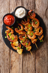 Fresh kebabs made from shrimps and pineapple slices decorated with green onions served with sauces...