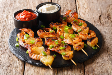 Grilled seafood kebabs from shrimp and pineapple slices with sauces close-up on a slate plate on a...