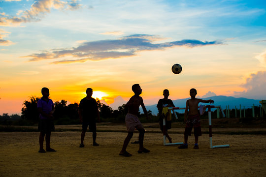 An action picture of a group of kid playing soccer football for exercise in community rural area under the sunset.
