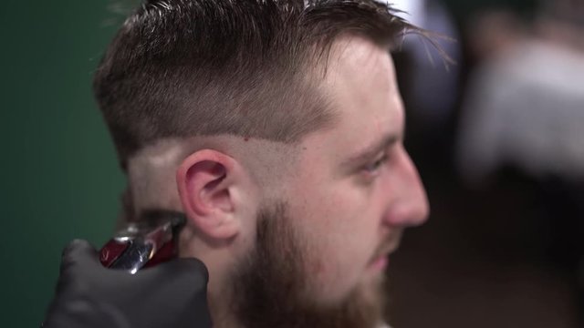 Barber is making haircut to the man with scissors and comb