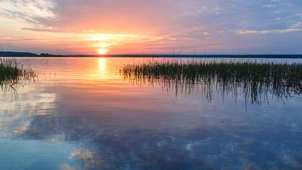 Obraz premium The rays of the dawn sun on the lake. Reflection of sunset clouds in the river. Rural landscape.