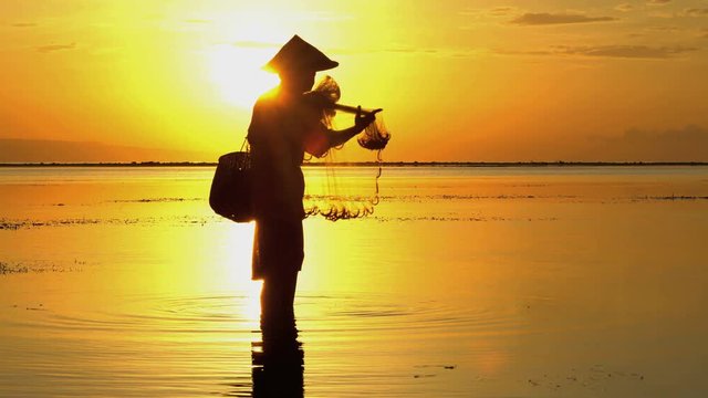 Balinese fisherman in silhouette throwing net into the ocean on a sunrise beach