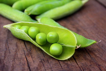 A lot of peas on the wooden table are closed and open pods. Green ripe peas close-up, organic food.