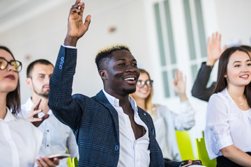 I have a question. Group of people sitting at the chairs in conference hall, raising their hands. Workshop at university. Business and Entrepreneurship event.