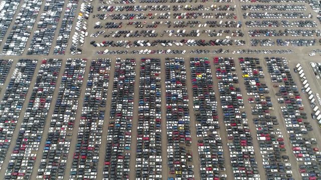Aerial footage of automaker car distribution lot with vehicles parked close to each other different colors and types also showing cars driving over area for finding space to park 4k high resolution