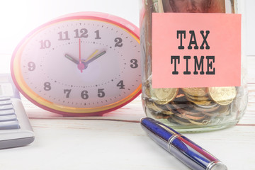 TAX DAY CONCEPT; Clock,red note,calculator and coins in the mason jar over wooden background.