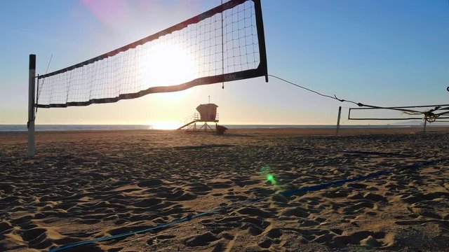 Low fly to empty volleyball nets with beautiful sunset and lifeguard tower in distance, aerial 4k drone in Huntington Beach, CA
