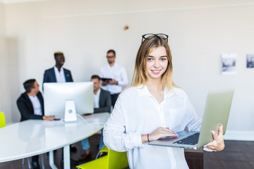 Portrait of pretty cheerful business woman in an office environment holding laptop.