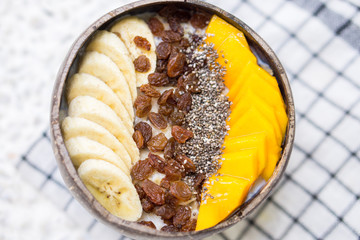Oatmeal with banana, raisins, mango and chia seeds in coconut bowl