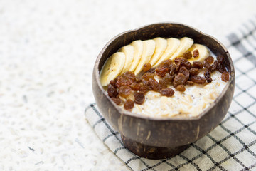 Oatmeal with banana, raisins and chia seeds in coconut bowl
