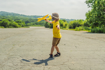 Happy kid playing with toy airplane against old runway background. Traveling with kids concept