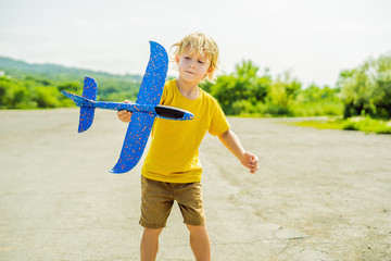 Happy kid playing with toy airplane against old runway background. Traveling with kids concept