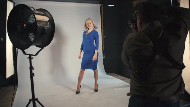Photo shoot beautiful blonde woman in a blue dress on white studio backdrop.
