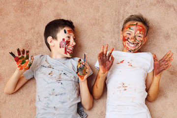 little cheerful boys with paint on face and hands lying on floor and laughing.