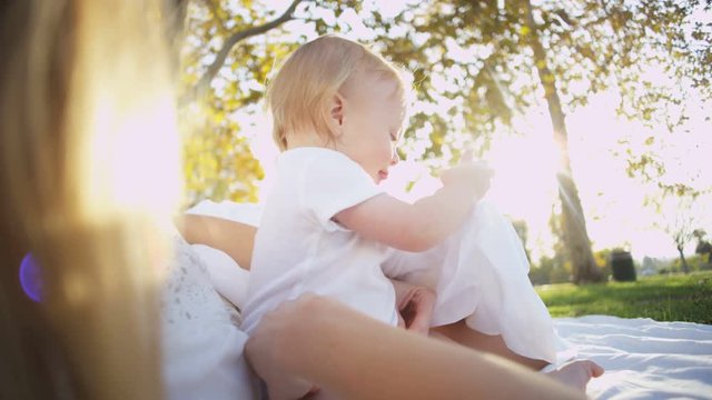 Beautiful blonde young European mother lying outdoors in the park playing with her young baby boy 