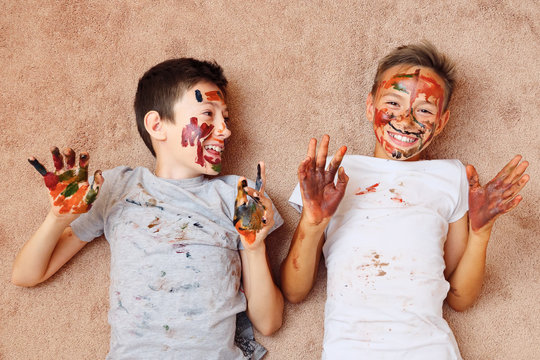 little cheerful boys with paint on face and hands lying on floor and laughing.