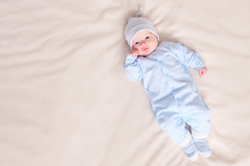 From above shot of cute baby in warm pajamas and hat lying on comfortable bed at home, copyspace