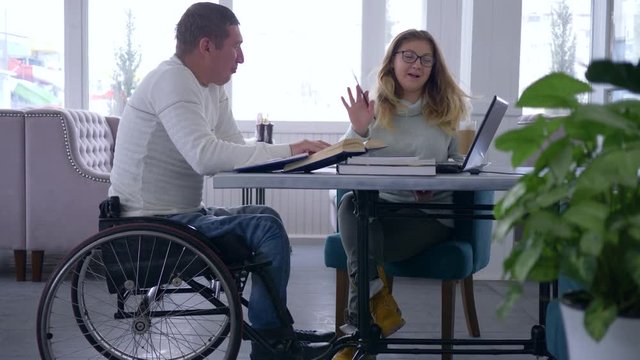 education for handicapped, diseased student senior man in wheelchair with tutor women during home teaching courses using laptop computer in restaurant