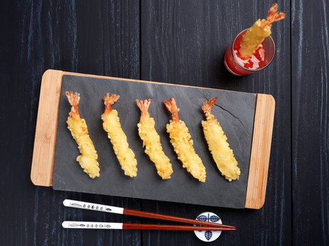 Shrimps tempura with sweet chili sauce on black slate board, set on a dark blue background, top view