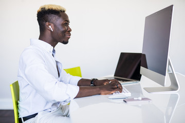 Afro american businessman sitting at office desk, working on desktop computer.