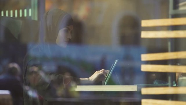 Attractive lady in hijab working on tablet, sitting in cafe, freelance project