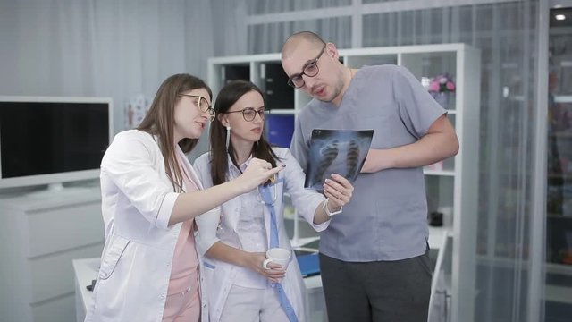 A group of doctors checking X-rays and drinking a hot drink in the staffroom room. The doctor looks at the x-ray picture with ribs and chest