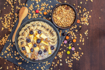 Oatmeal with bananas, blueberries and apple on dark wooden table. Top view.