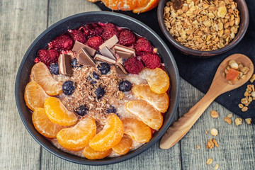 Oatmeal with tangerine, blueberries, chocolate and raspberry on grey background. Top view.