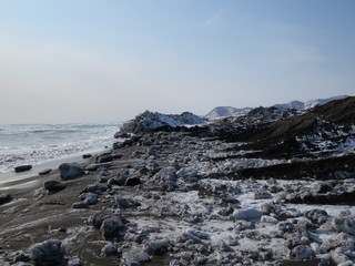 Pacific Ocean, waves and views of the snow-covered hill in winter in sunny weather in Kamchatka, Russia